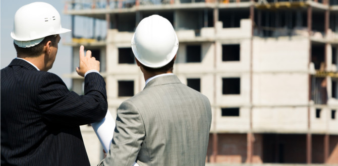 Photo of successful architect pointing to the building with foreman near by